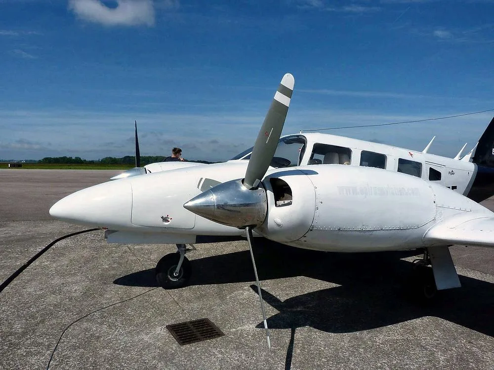 A close-up view of the front of a white Piper PA-34 Seneca II, N4387F, showing the propeller and nose on a sunny day.