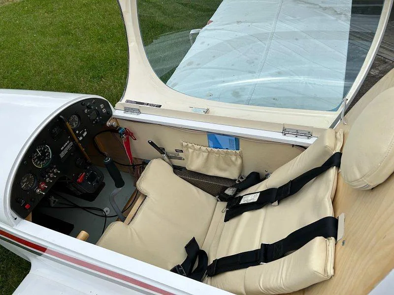 The beige interior cabin of a light sport aircraft, showing the seats with harnesses and a partial view of the instrument panel.