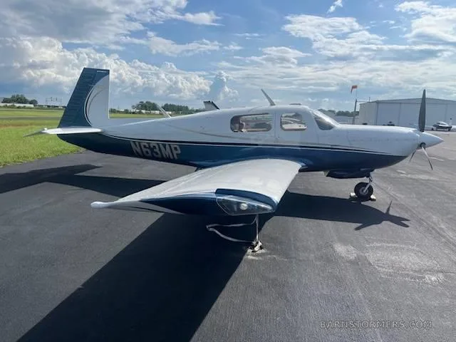 A white and blue single-engine propeller aircraft (N63MP) parked on an asphalt ramp with a propeller visible, under a partly cloudy sky.