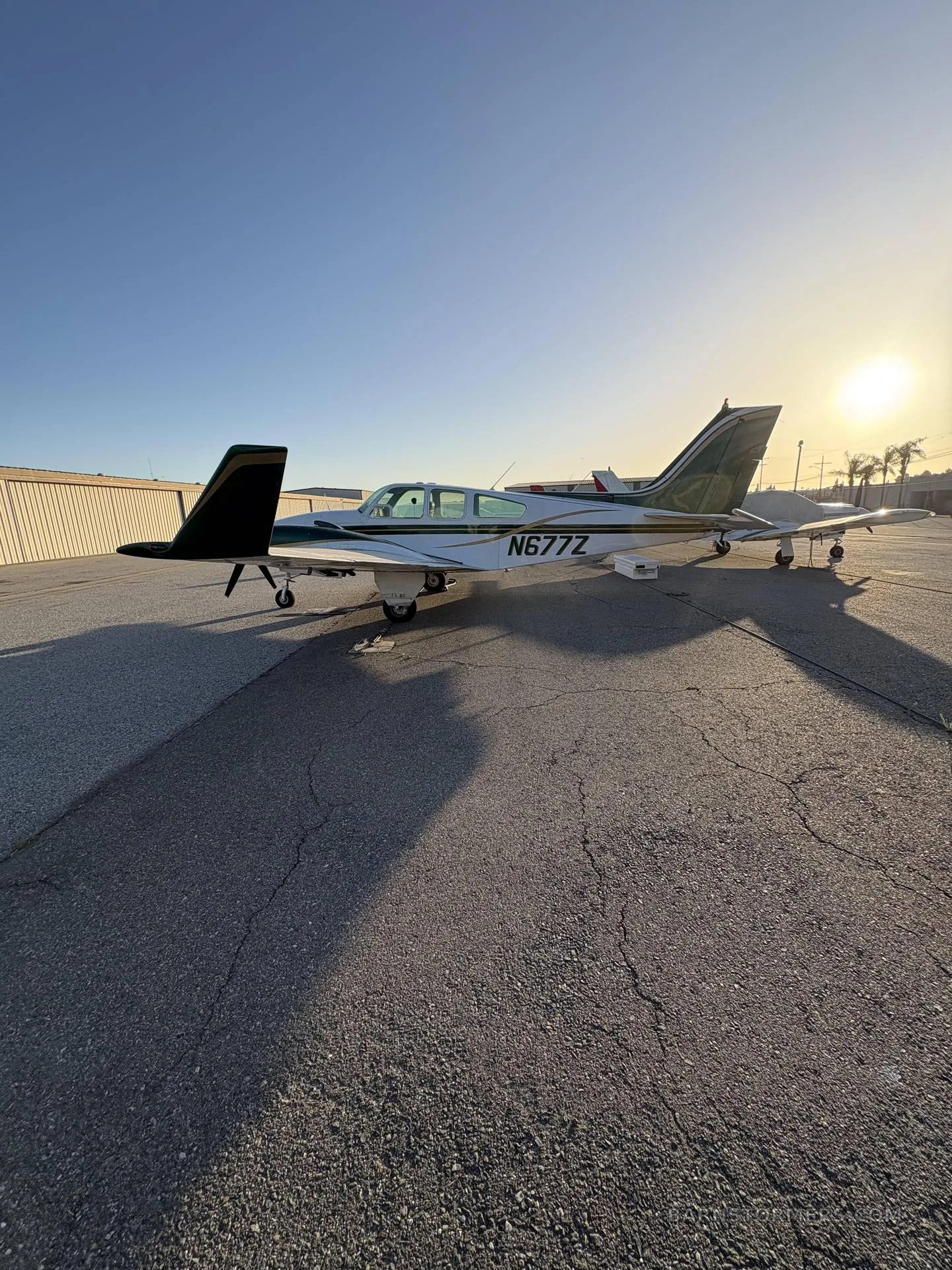 A white and green twin-engine propeller aircraft (N677Z) parked on an asphalt ramp at sunset.