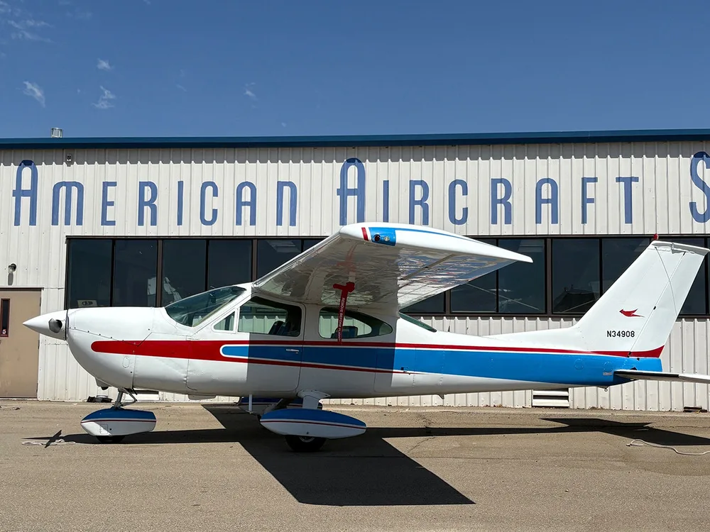 A side view of a white Cessna 177 Cardinal with blue and red stripes parked on an asphalt ramp.