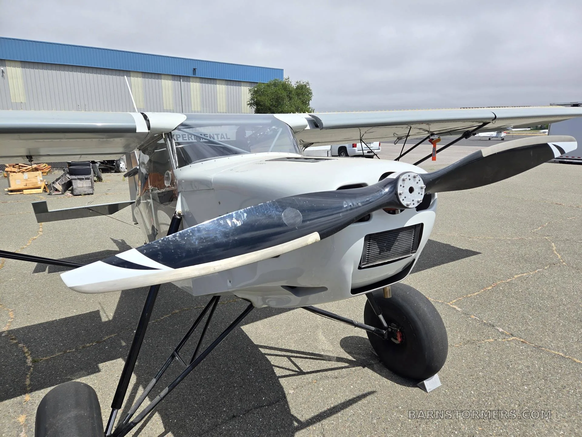 A close-up front view of a light gray and white high-wing aircraft with a propeller and large tires.