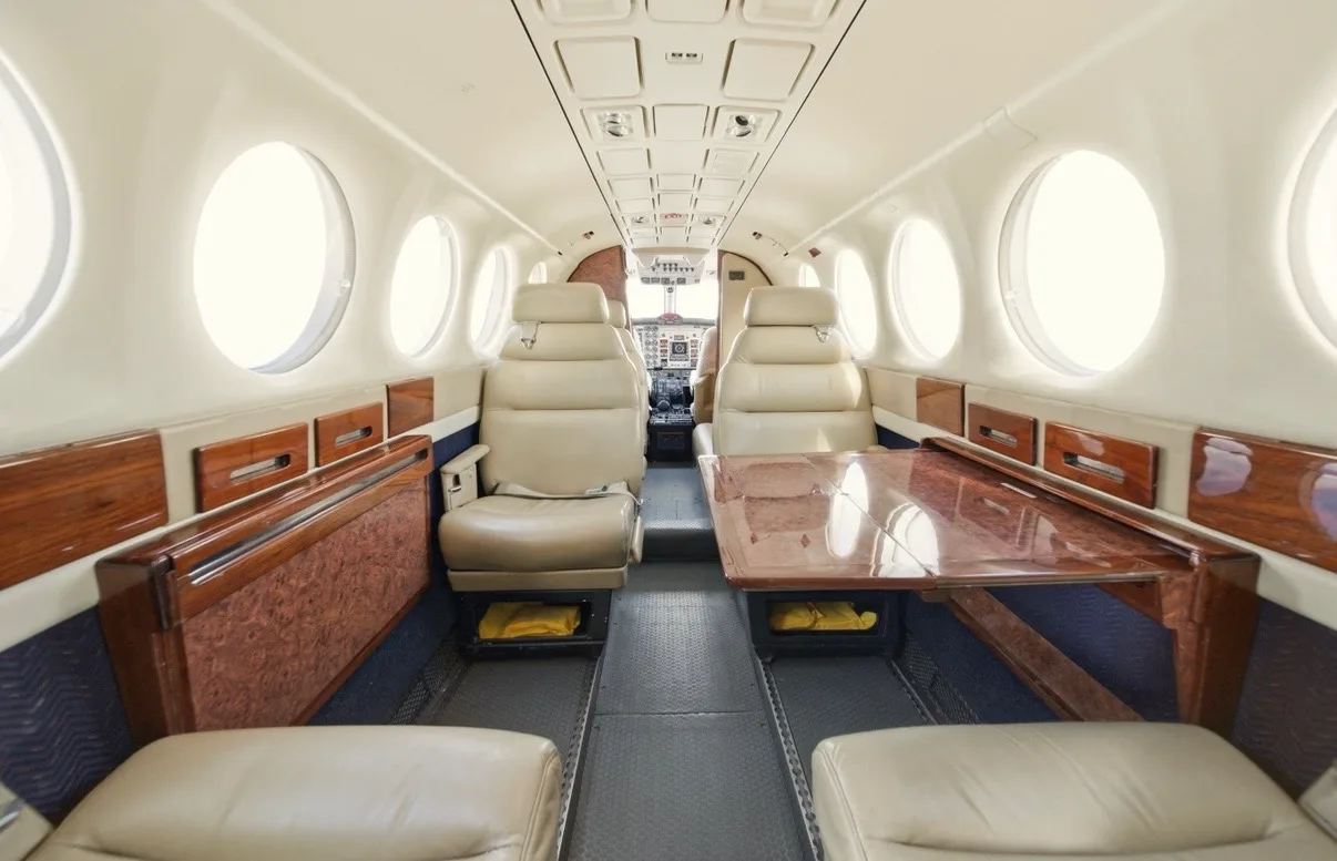 The aircraft's cabin interior features beige leather seating, wood paneling, and a central table.