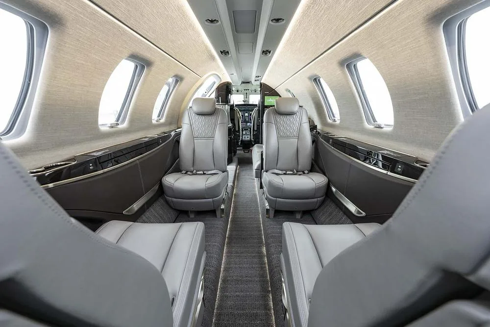 The aircraft's interior cabin with grey leather seats and a view towards the cockpit.