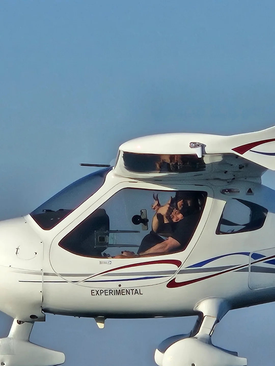 A white Flight Design CTLS light sport aircraft in flight, showing a pilot giving a thumbs-up from the cockpit.