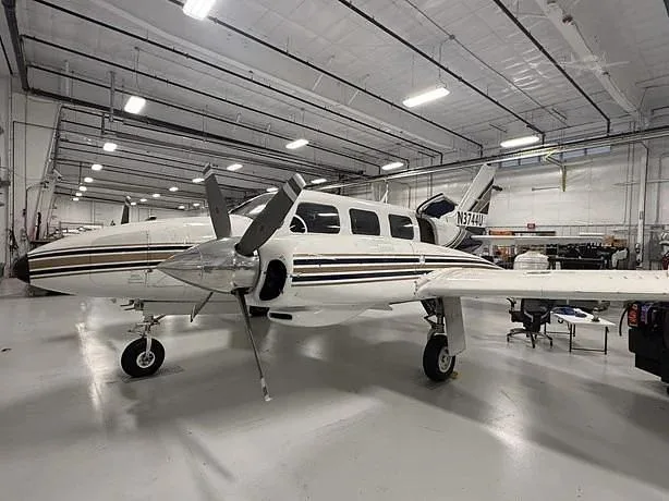 A white and blue twin-engine aircraft with registration N3744U and propellers is parked inside a hangar, viewed from the front-side.