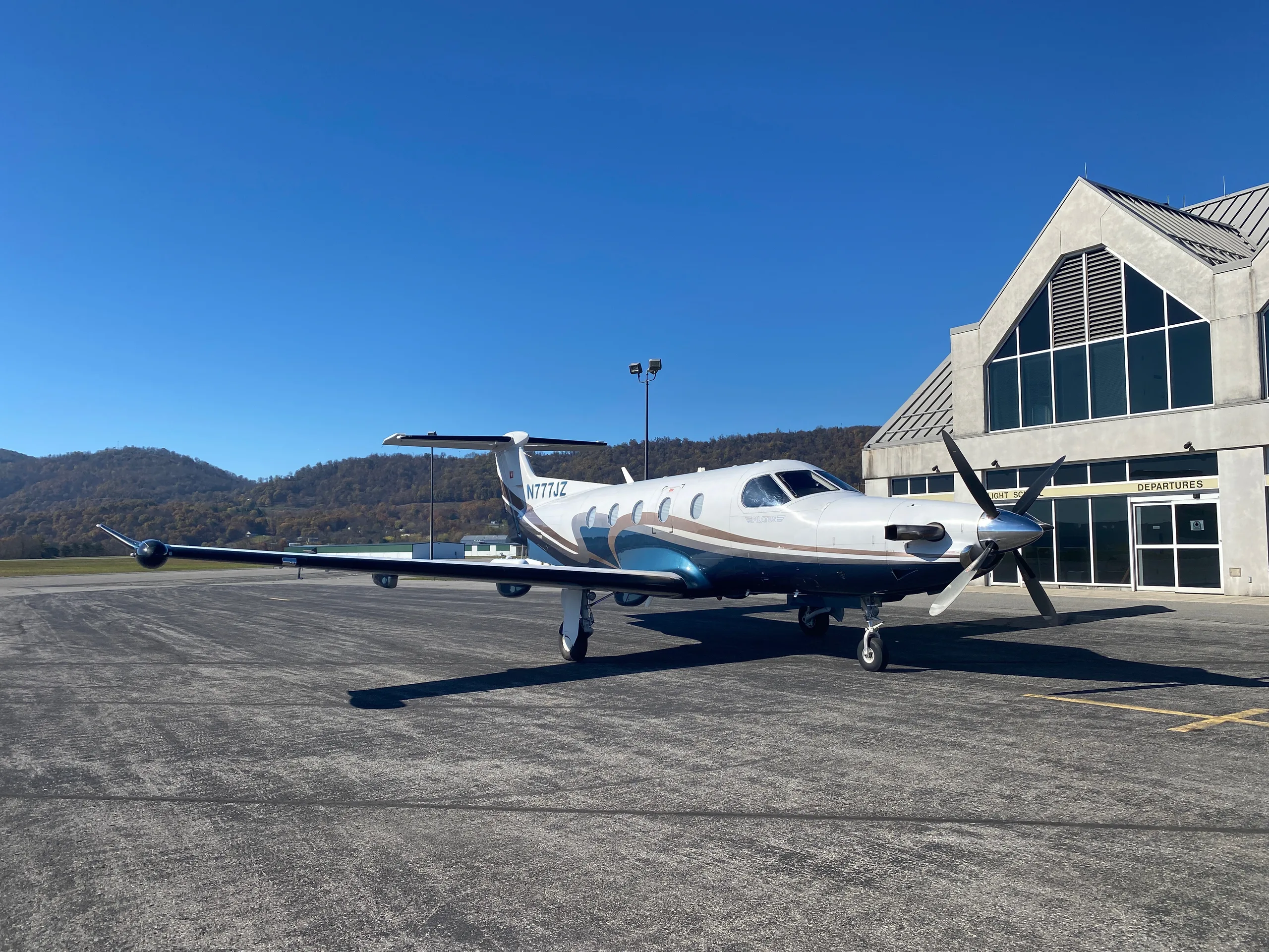 A Pilatus PC-12 aircraft with registration N777JZ is parked on the tarmac in front of a building.