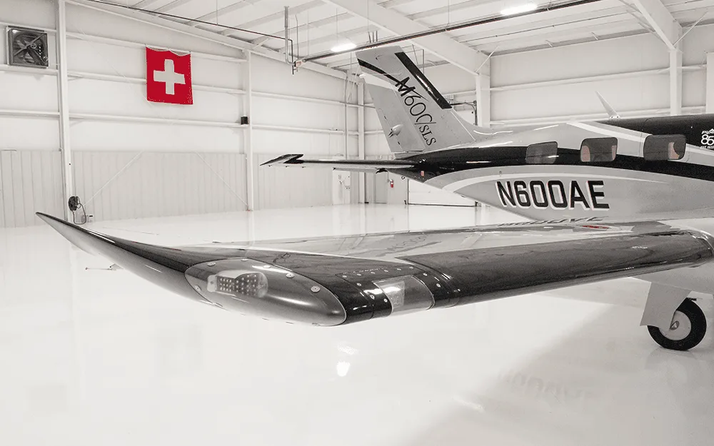A close-up view of the wingtip and tail of the Piper M600/SLS aircraft (N600AE) in a hangar, showing its black and silver livery.