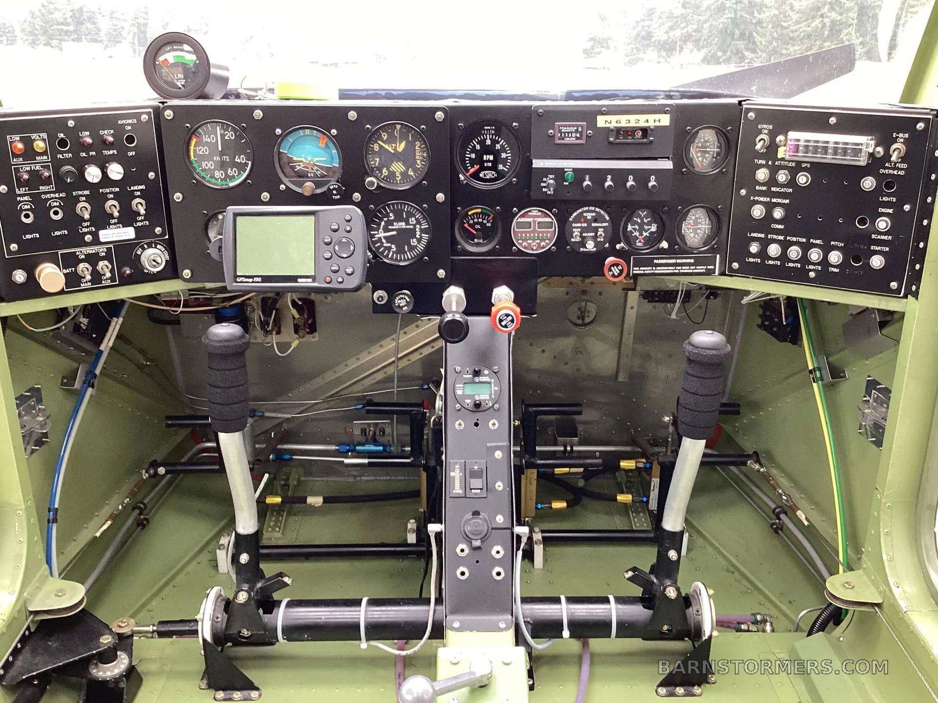 The cockpit of a floatplane, showing the instrument panel with various gauges, a GPS unit, and dual control sticks.