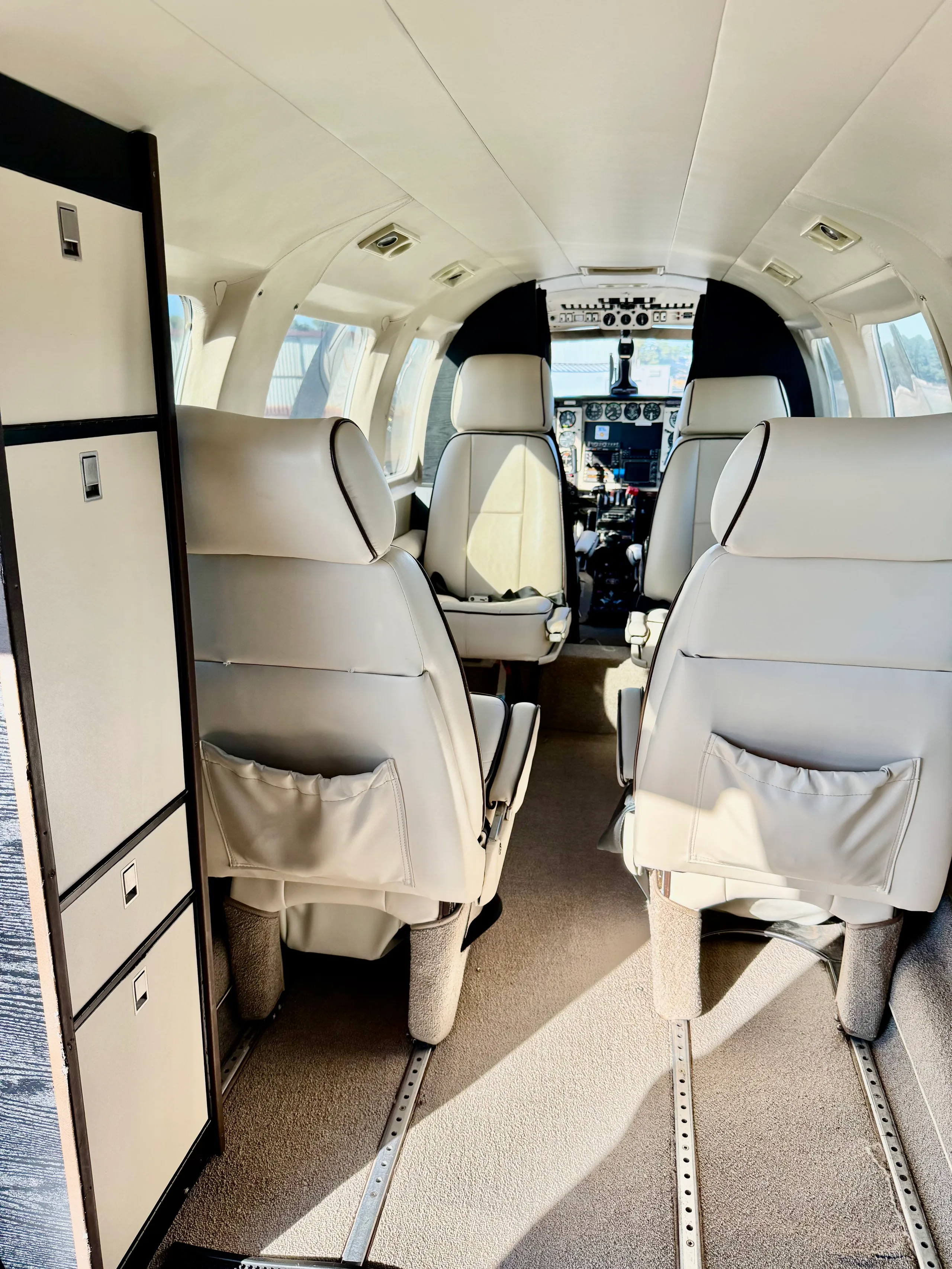 A view down the aircraft's cabin aisle, showing cream-colored seats and storage compartments.