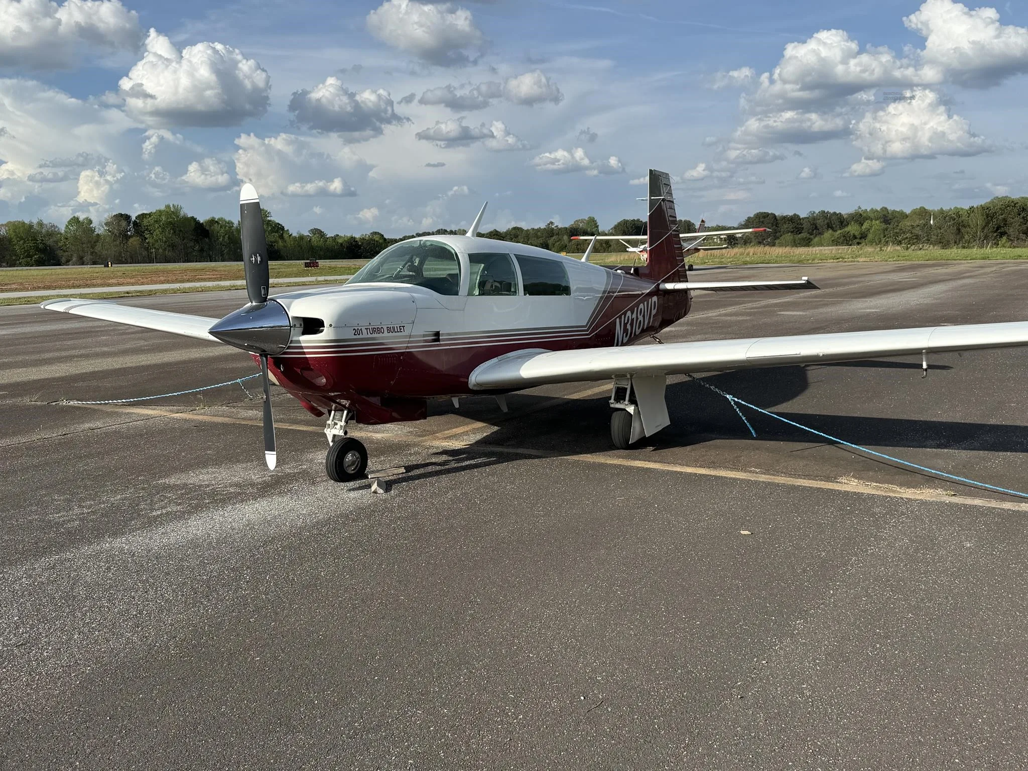 A red and white Mooney 201 Turbo Bullet aircraft, N318VP, parked on an asphalt ramp, viewed from the front-right.
