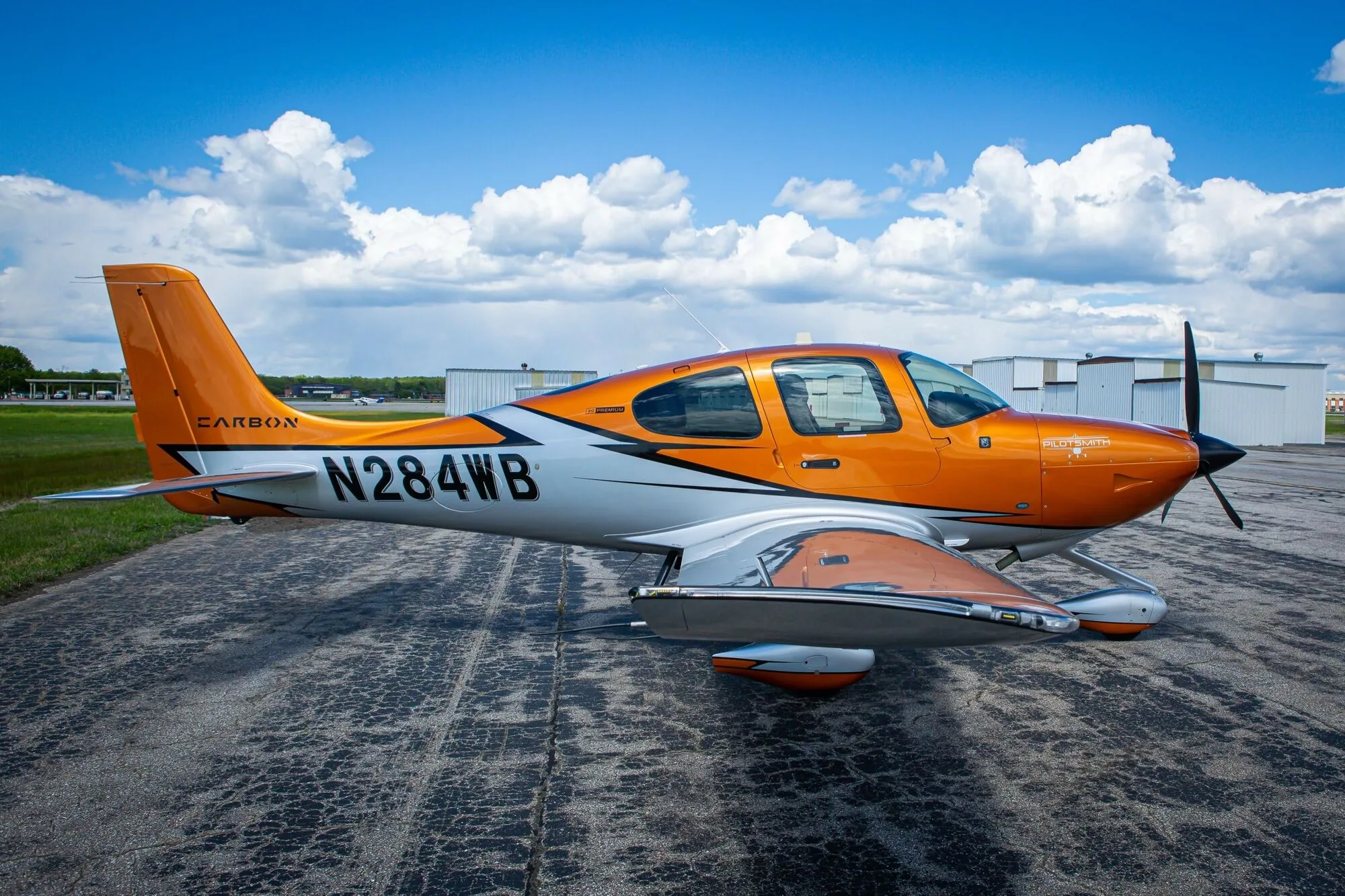 A side view of an orange and silver Cirrus SR20 aircraft, N284WB, parked on an airfield under a blue sky.