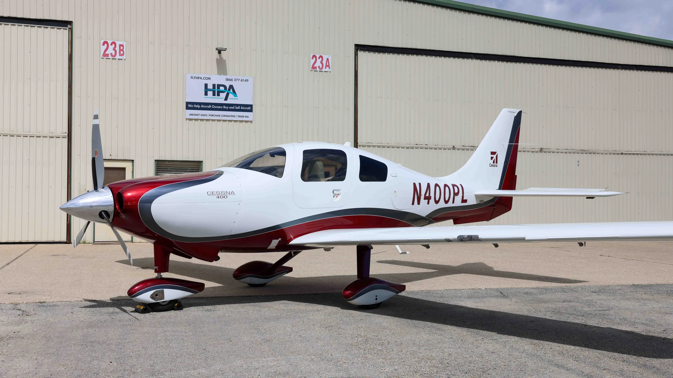 A white and red Cessna 400 aircraft, N400PL, parked in front of hangars.