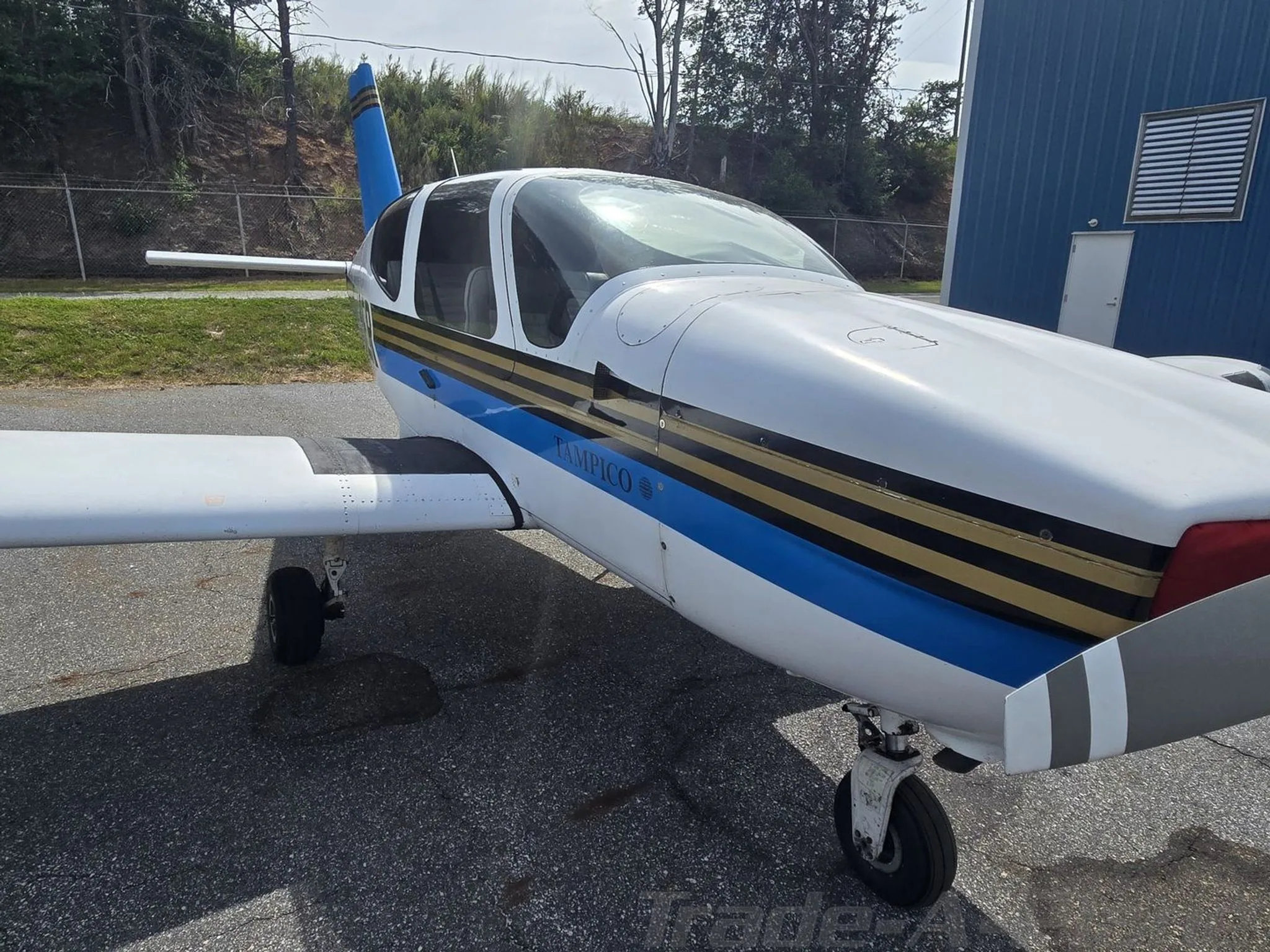 A front-side view of the white and blue Socata TB-9 Tampico N130ER parked next to a blue hangar.