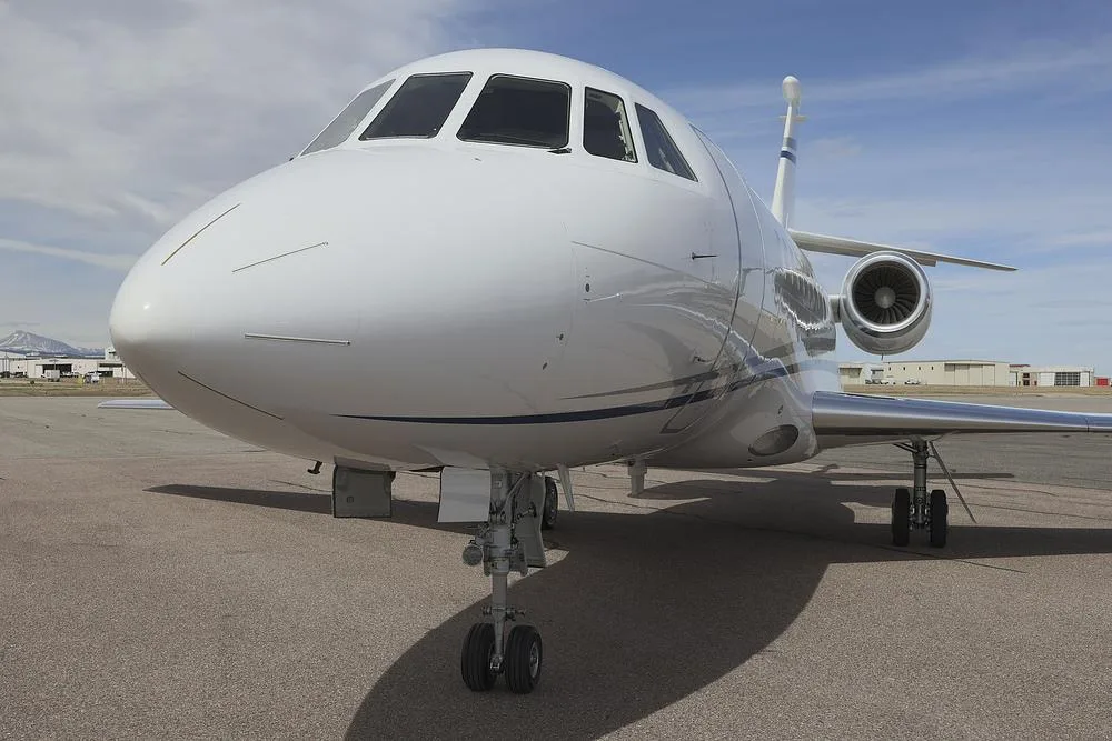 A close-up, low-angle view of the nose and cockpit of a white Dassault Falcon 900 business jet with blue stripes.