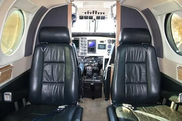 View from the aircraft cabin showing two black leather pilot seats and the cockpit instrument panel beyond.