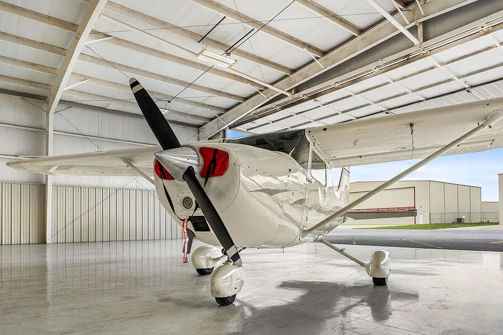 A front-quarter view of the white Cessna 172, registration N5268H, with red propeller covers, inside a hangar.