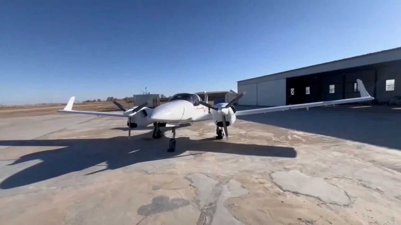 Front view of a Diamond DA42 aircraft parked in front of a hangar.
