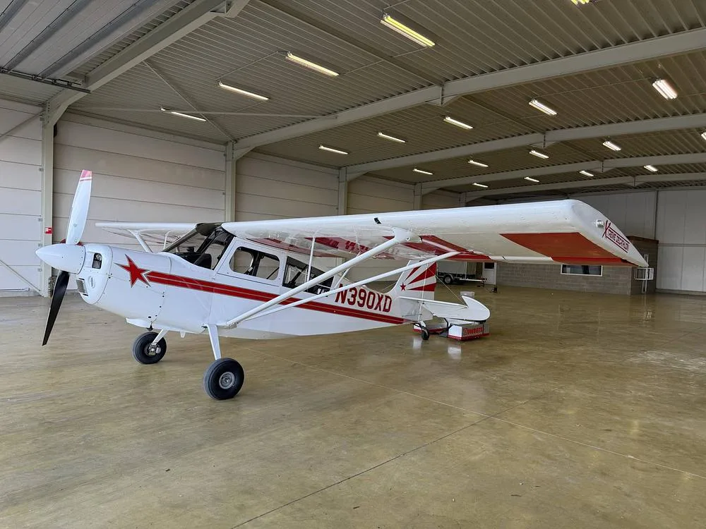 A white single-engine aircraft with red stripes and a red star on the tail, parked inside a hangar.