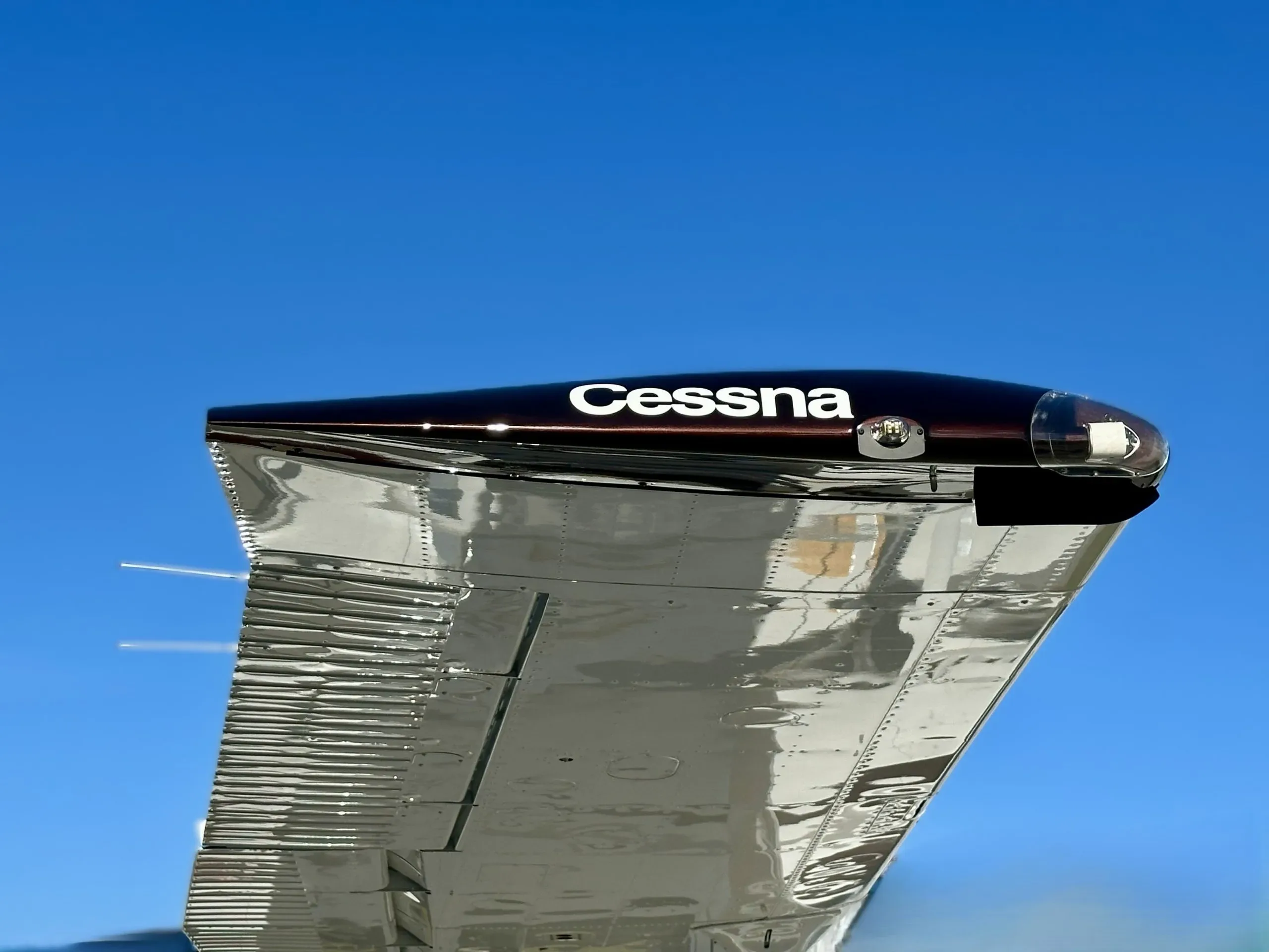 A close-up of the polished metal wingtip of a Cessna aircraft against a blue sky.