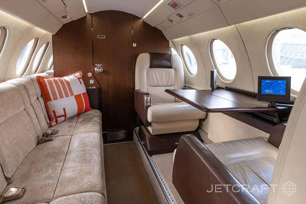 A section of the business jet cabin interior featuring a beige sofa, a single cream leather seat, and a small table.