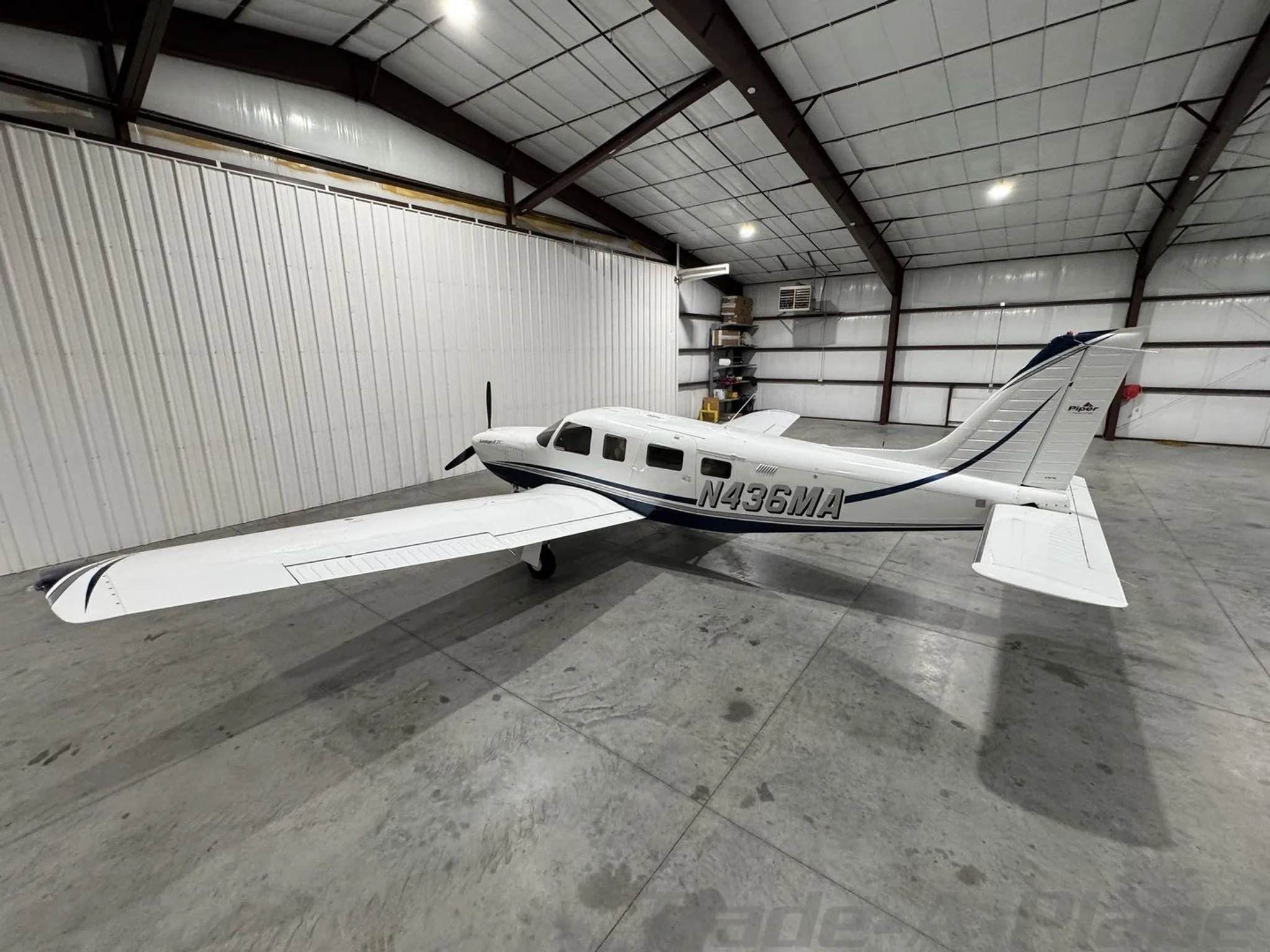A side view of the white Piper Saratoga II TC N436MA with blue stripes inside a hangar.