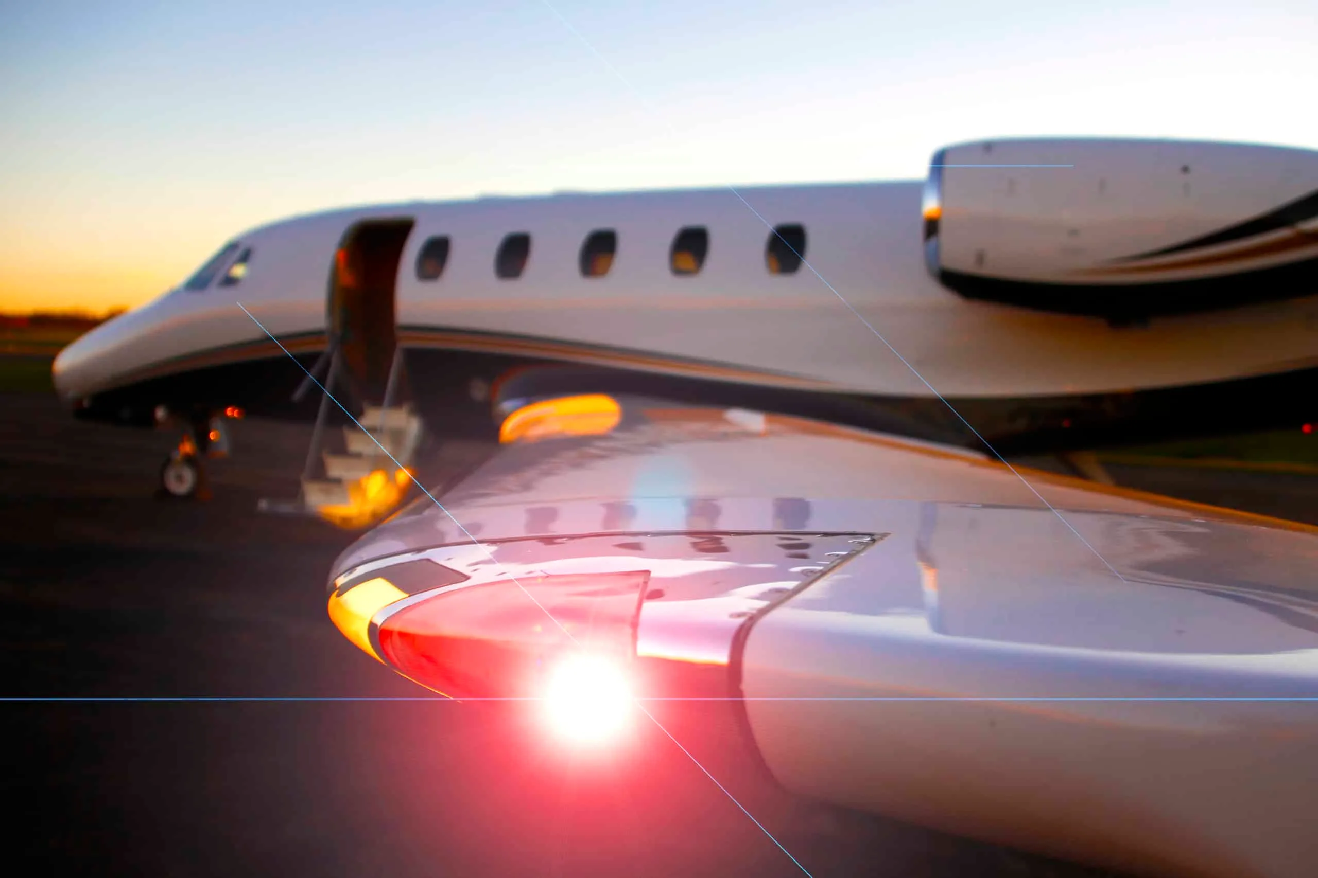 A close-up view of the wingtip and landing lights of a white business jet with its passenger door open at dusk.