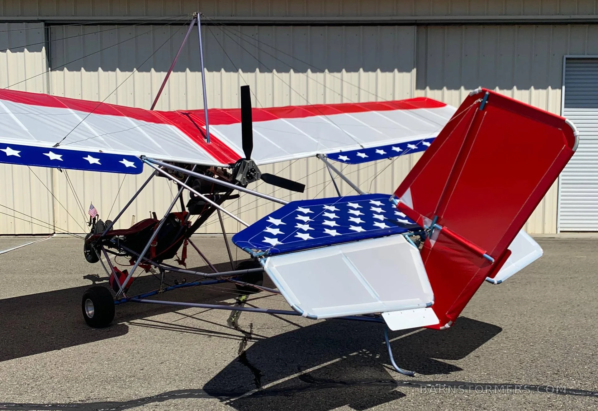 An ultralight aircraft with a red, white, and blue American flag paint scheme parked on an airfield.