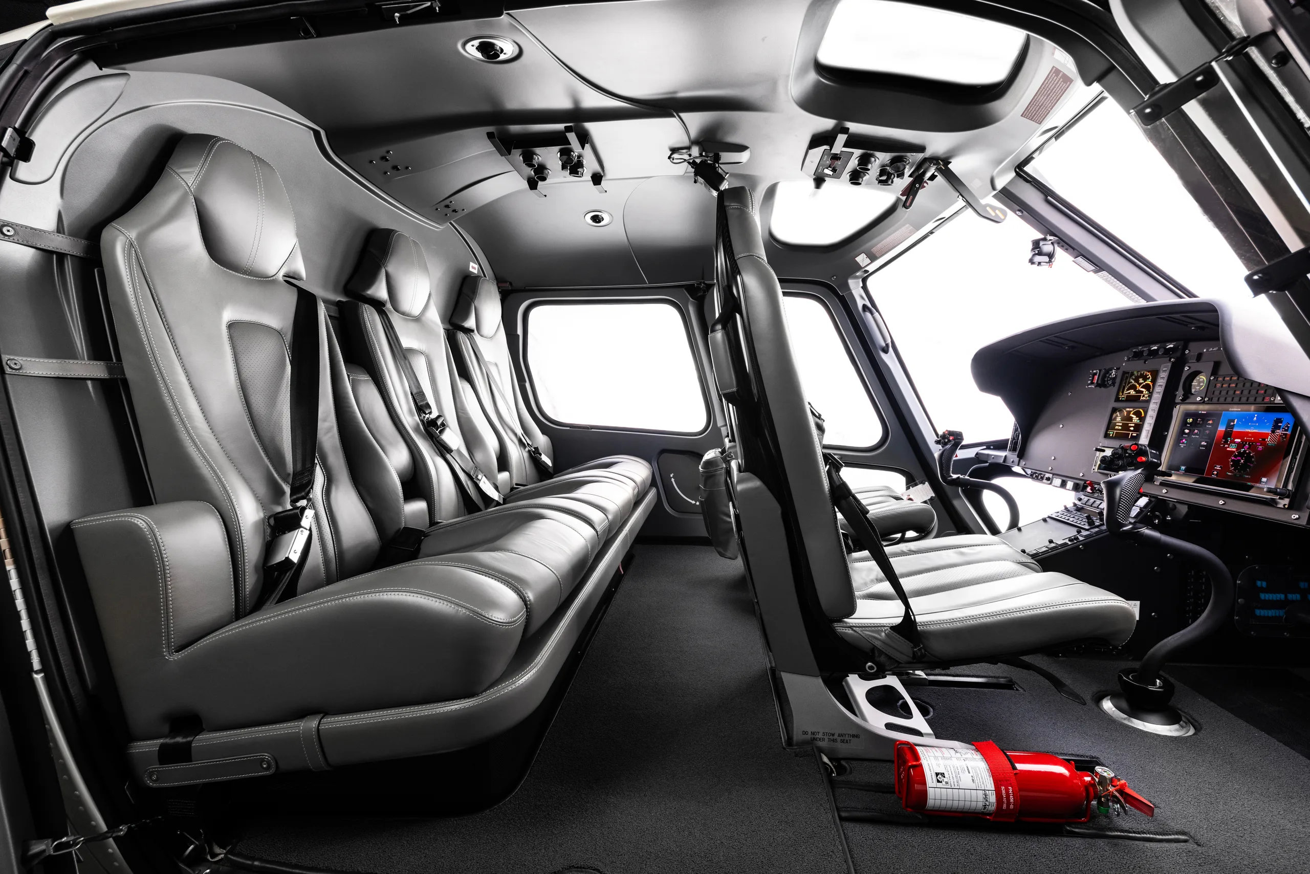 The grey leather interior cabin of a helicopter with seats and a partial view of the cockpit.