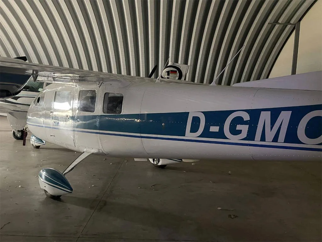 The fuselage of a white and blue Partenavia P.68 aircraft with registration D-GMC (partially visible) inside a hangar.