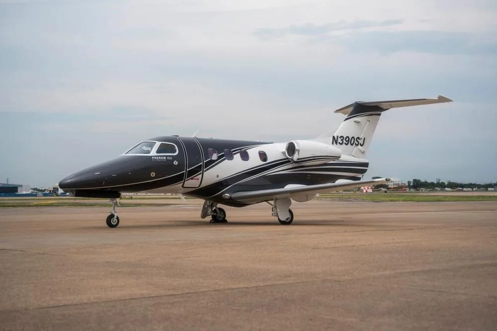 A black and white Embraer Phenom 100 business jet (N390SJ) parked on an airport tarmac under a cloudy sky.
