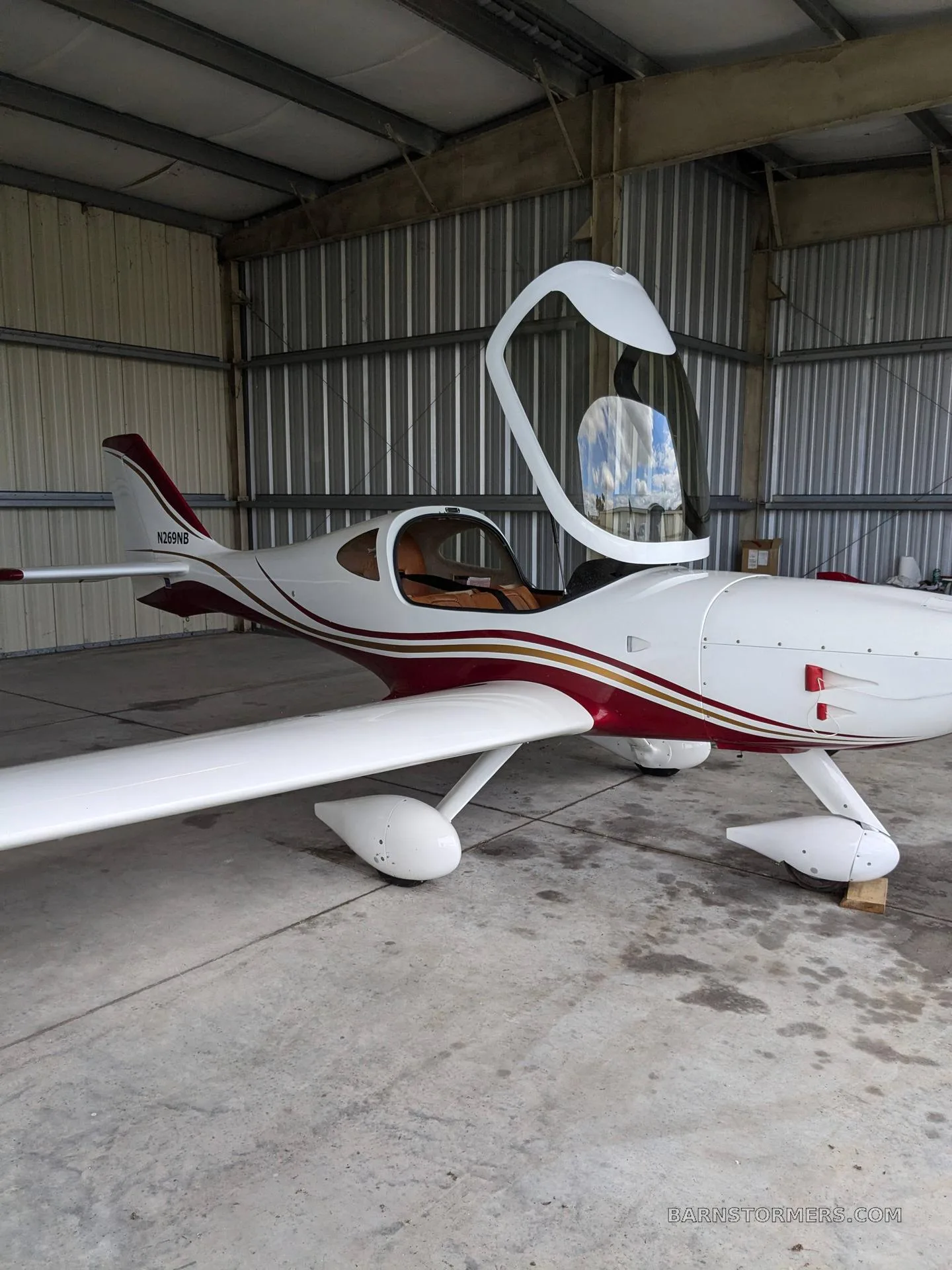 A white and red aircraft with an open canopy is parked inside a metal hangar.