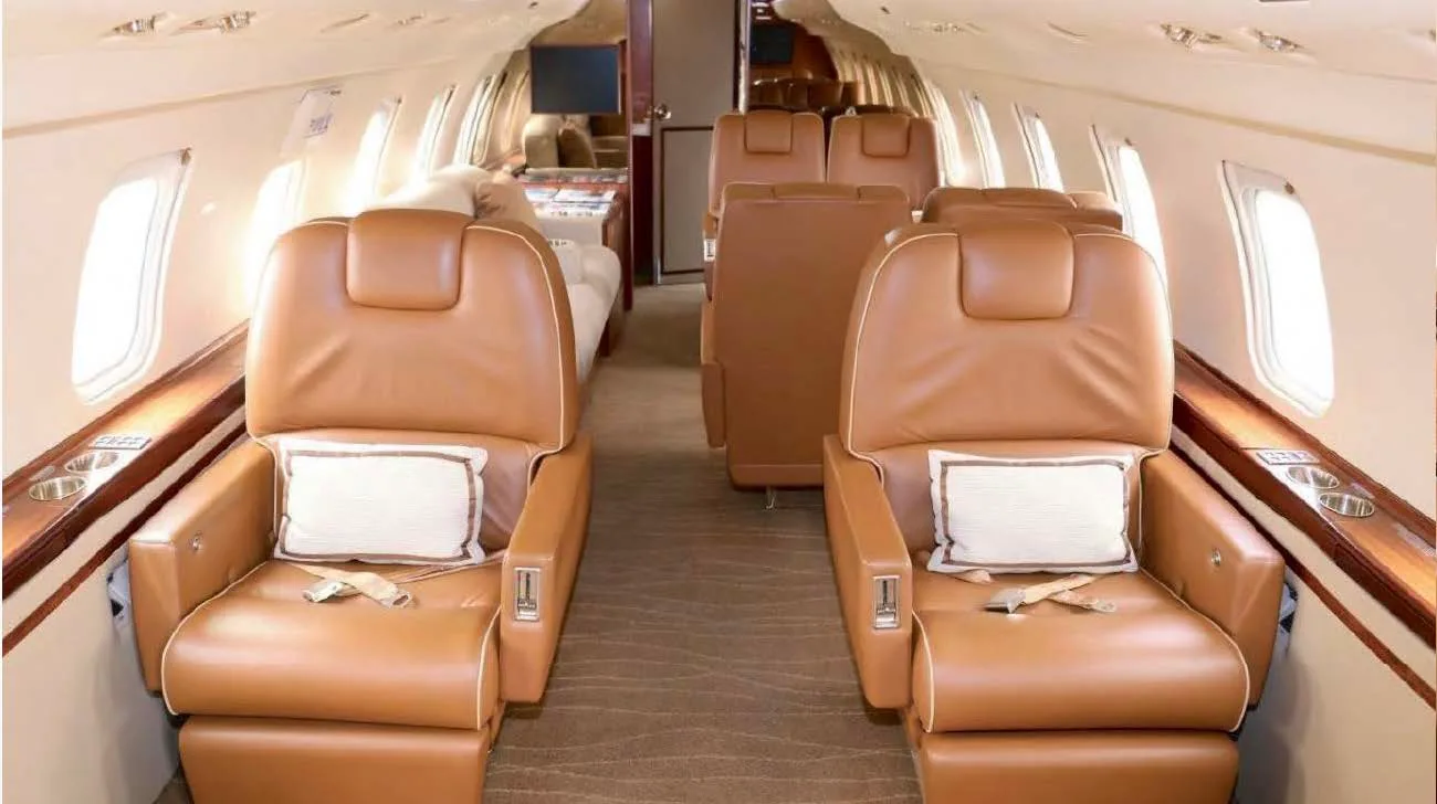 The interior cabin of a business jet with two rows of tan leather seats facing each other.