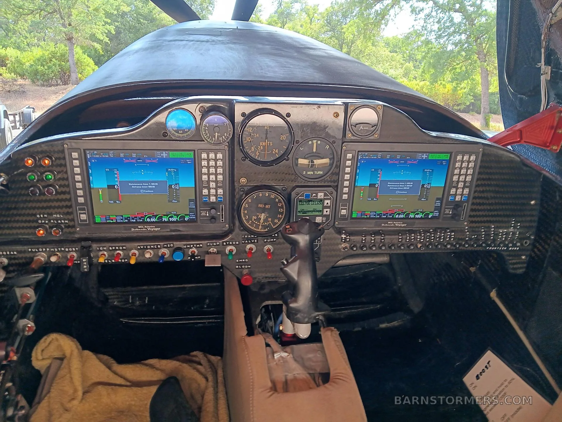 The cockpit of a dark aircraft, featuring a carbon fiber panel with multiple digital displays and analog gauges.