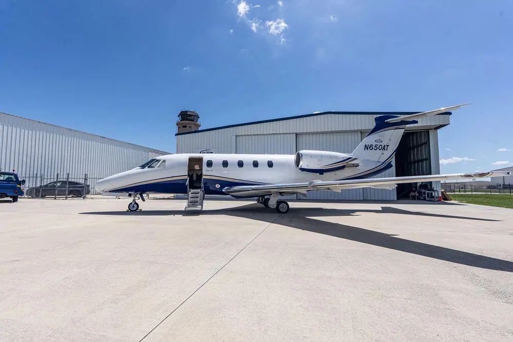 A white and blue Cessna Citation III business jet, N650AT, parked on an airfield with its door open, next to a hangar and control tower.
