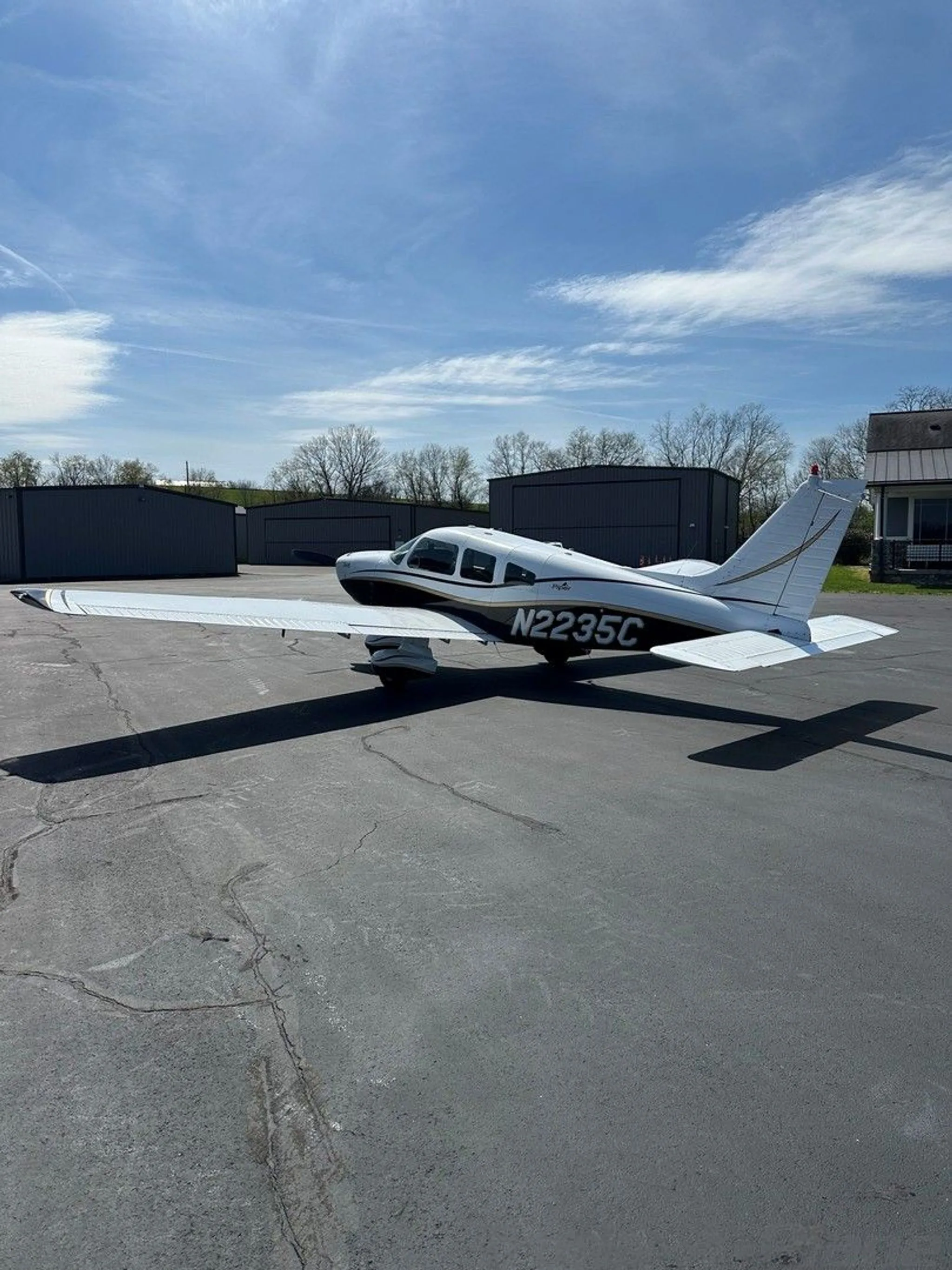 A white and black Piper aircraft with gold trim, registration N2235C, viewed from the rear-right on an asphalt ramp.