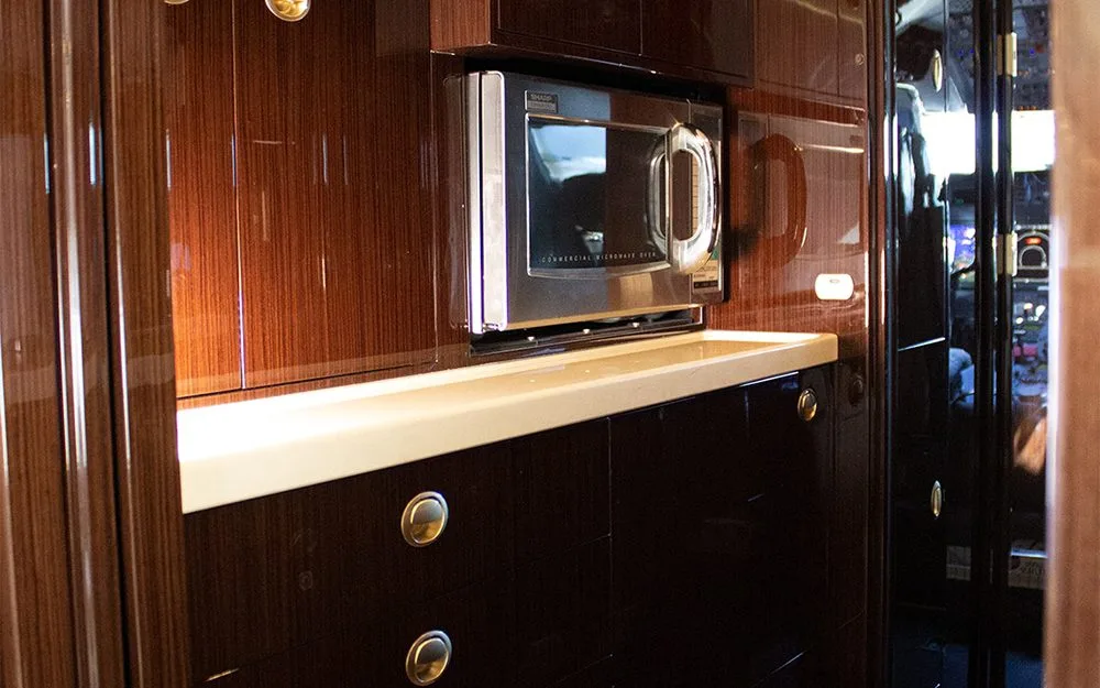 A close-up of an aircraft galley featuring a built-in microwave and dark wood cabinetry.
