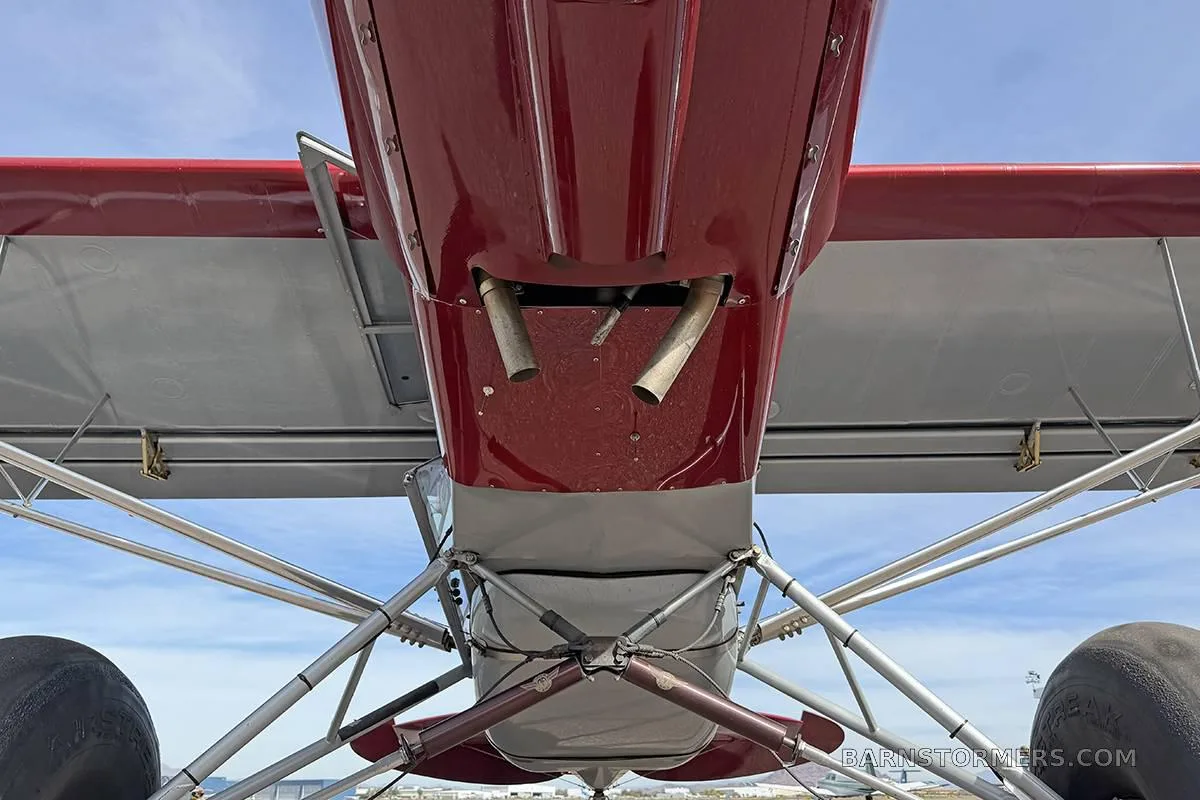 A view from directly underneath the red and grey aircraft, showing the landing gear and exhaust pipes.
