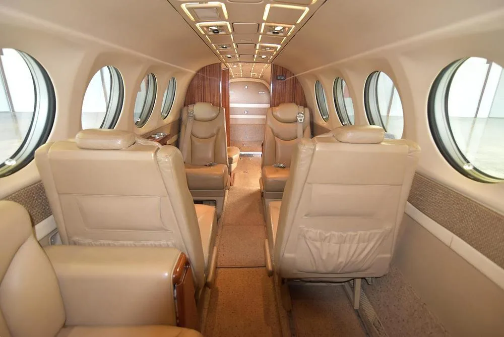 The aircraft's cabin interior features tan leather seats arranged in a club configuration with wood paneling.