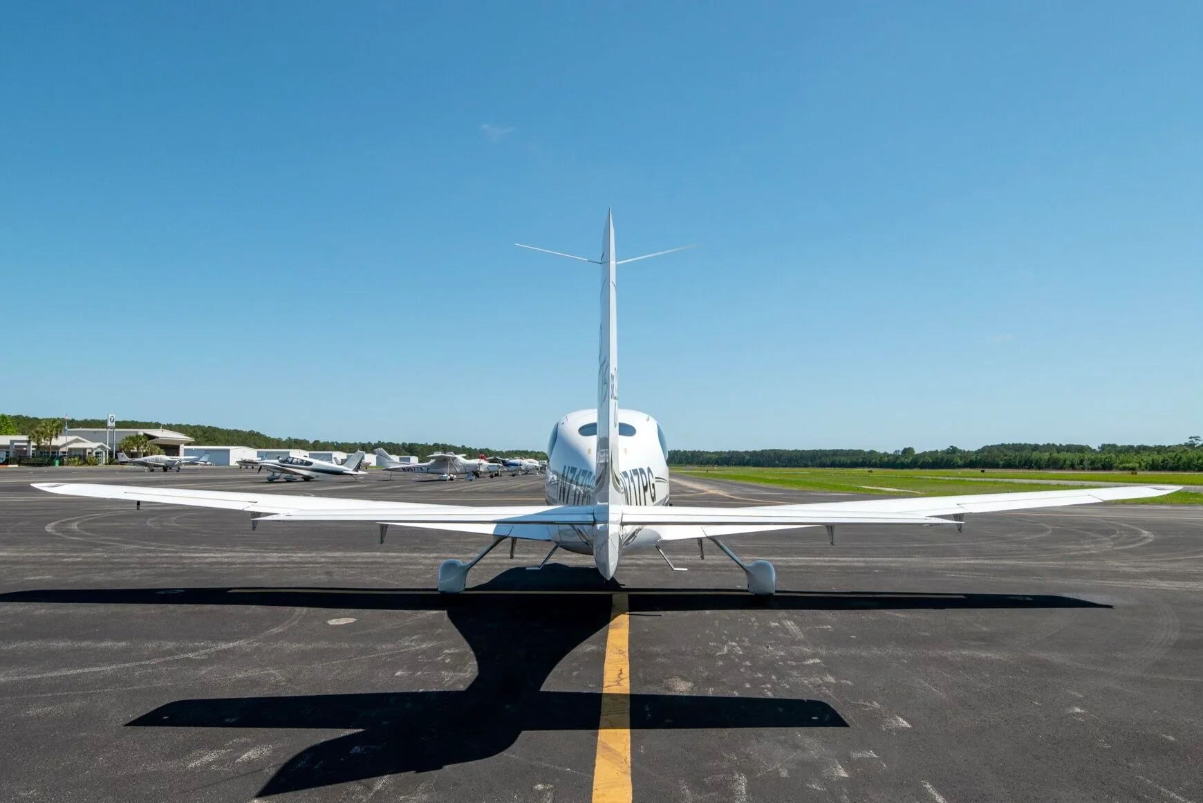 Rear view of a white Cirrus SR22T aircraft N717PG with black and grey stripes parked on an airfield.