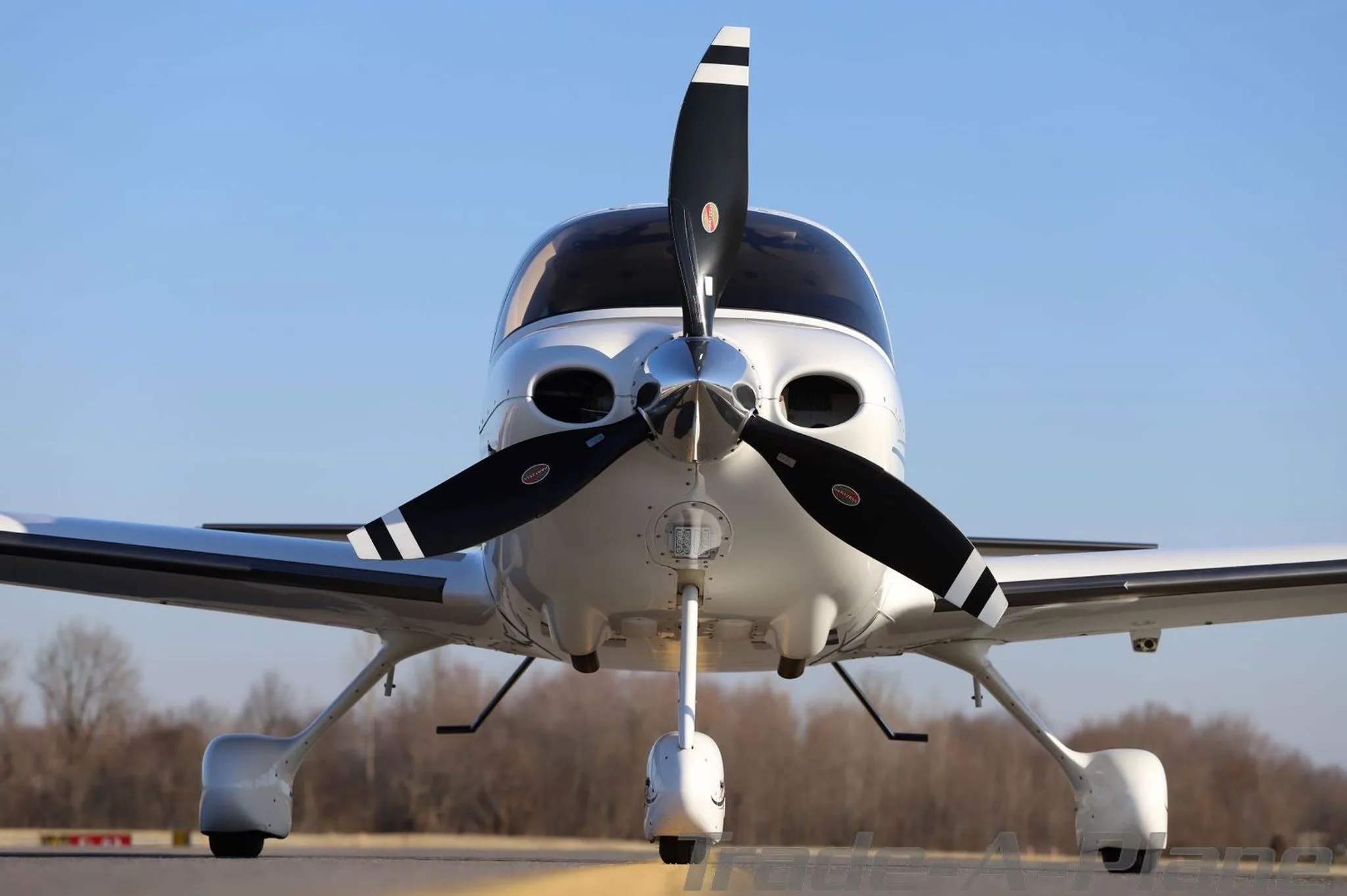 Front view of a white Cirrus SR22T aircraft with a black propeller, parked on an airfield.