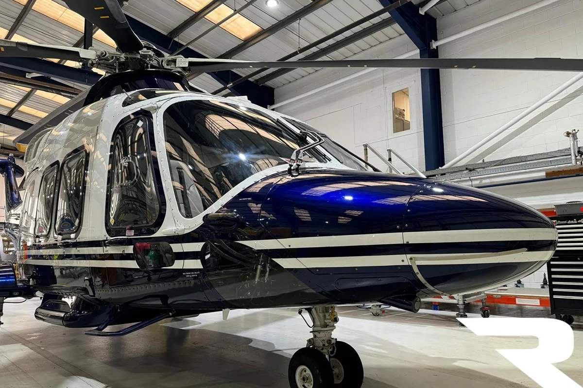Interior view of a helicopter cabin with blue leather seats and wood trim, looking towards the rear.