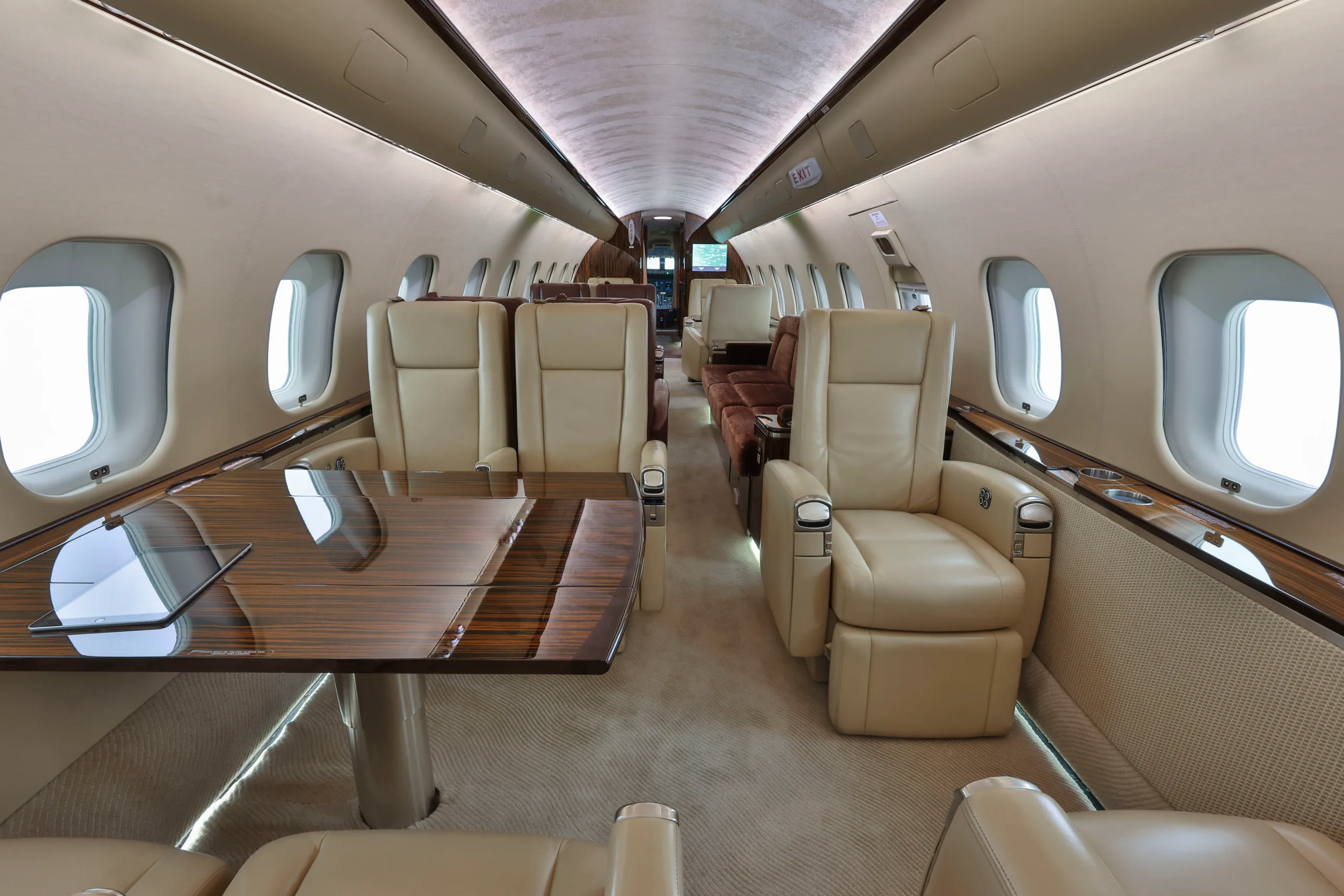 The spacious cabin interior of a business jet, with multiple beige leather seats and a large polished wooden table.