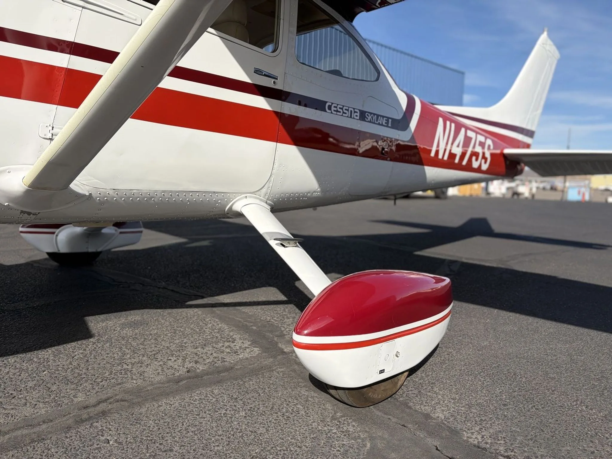 A low-angle side view of the main landing gear and rear fuselage of the white and red Cessna Skylane II (N1475S).