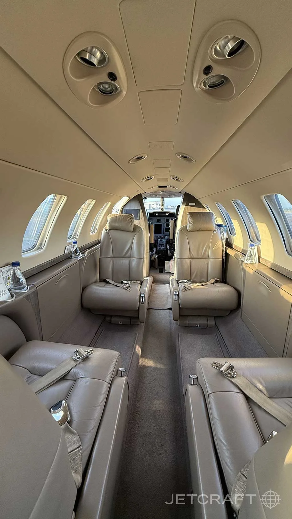 The interior of a business jet cabin with light tan leather seats and a view towards the cockpit.