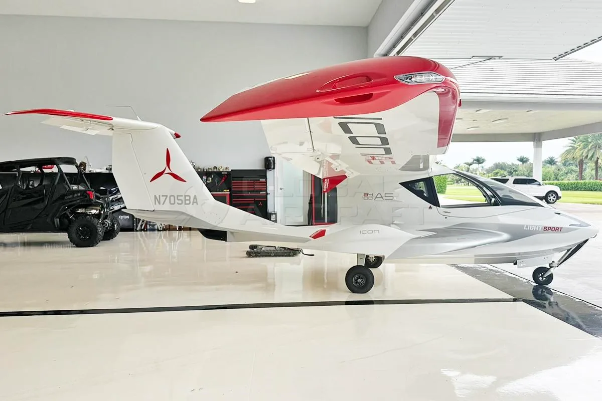 Side view of a white and red Icon A5 amphibious light sport aircraft with wings folded, inside a hangar.