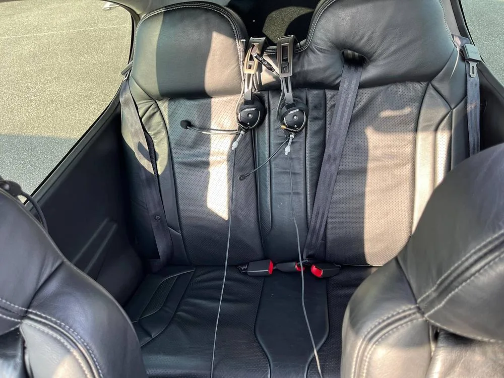 The black leather rear seats of a Cirrus SR22T aircraft cabin, with two headsets hanging.