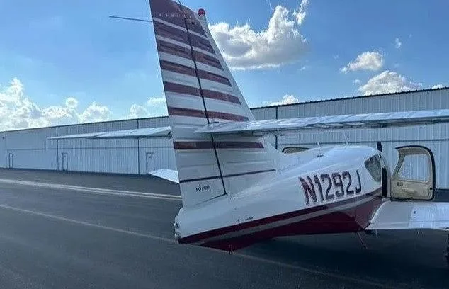 A rear-side view of the white and red aircraft N1292J, showing its tail and open door, parked next to a hangar.