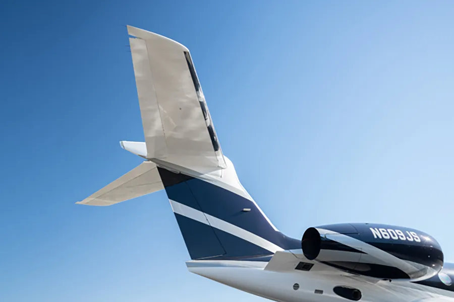 A close-up view of the tail and engine of a dark blue and white Gulfstream G650 business jet, tail number N609JS, against a blue sky.