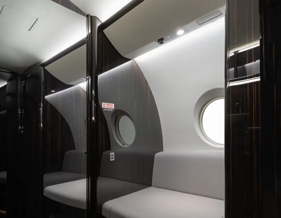 Aircraft cabin with white leather seats and dark wood accents.